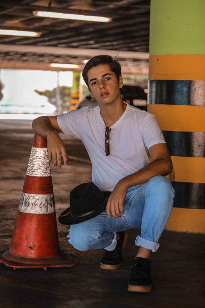 Man in White T-shirt Sitting Beside Traffic Cone